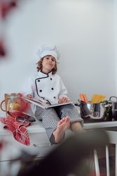 Delighted preteen boy sitting on kitchen counter with cookery bo