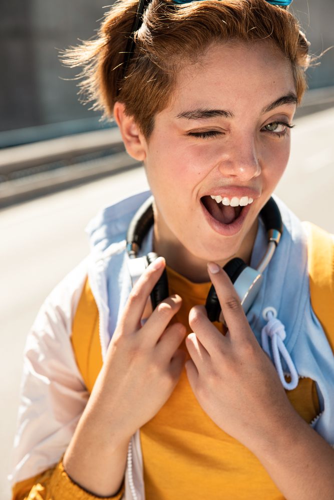 Playful trendy woman on street in sunshine covering camera with hands