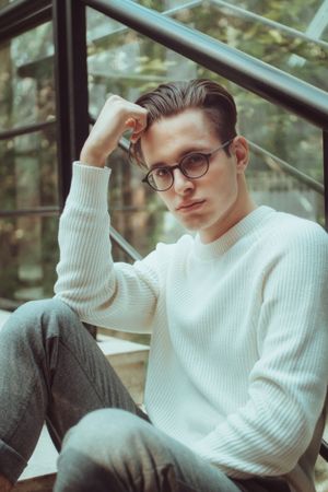 Portrait of man in light sweater wearing framed eyeglasses sitting outdoor