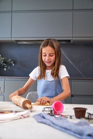 Positive girl with rolling pin kneading cookie dough