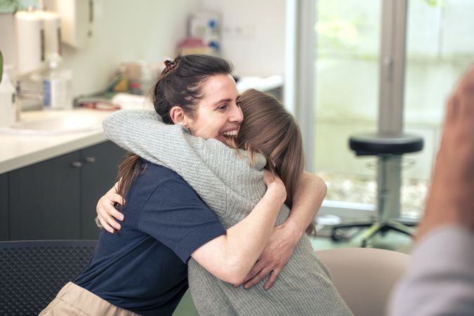 Happy lesbian couple hugging in a doctor's office after receiving good news.