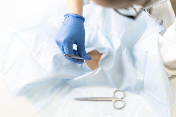 Young doctor with scissors and tweezers near hand of patient