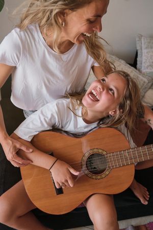 Woman teaching a girl to play the guitar while looking at each other laughing