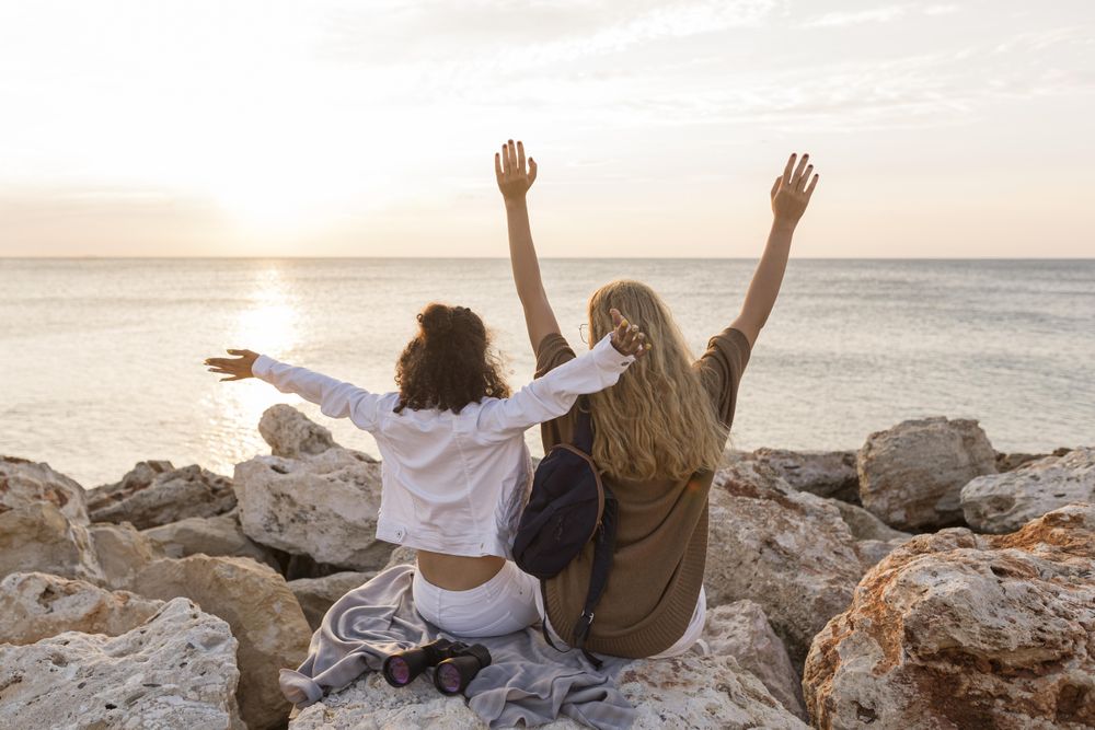 Rear view of two women sitting on rock near the sea
