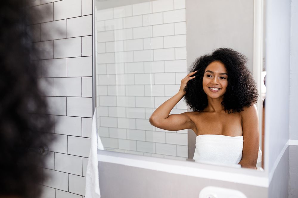 Happy Black woman and touching her hair before a shower