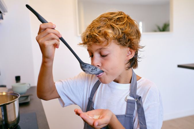Boy tasting sauce from spoon in house kitchen