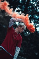 Young man holding red smoke standing near tree