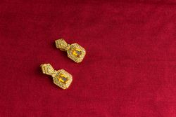 Beautiful shiny golden earrings with diamond studded Indian traditional design on a red velvet background
