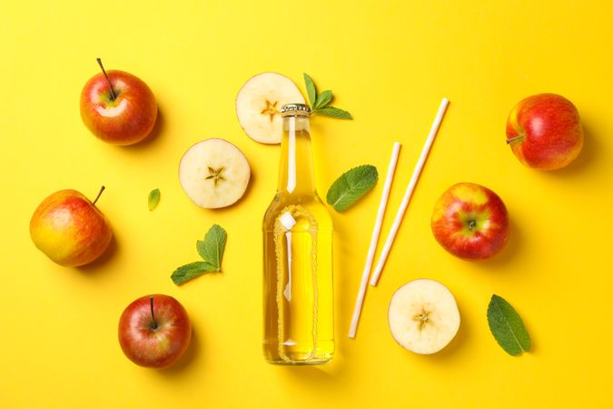 Composition with cider, apples and straws on yellow background