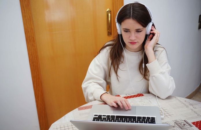 Teenage girl using headphones and laptop to attend an online class
