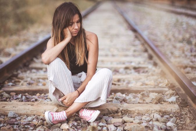 Long haired woman sitting on railways overgrown with dry grass