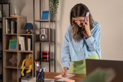 Woman on a phone call writing notes at a desk in a home office