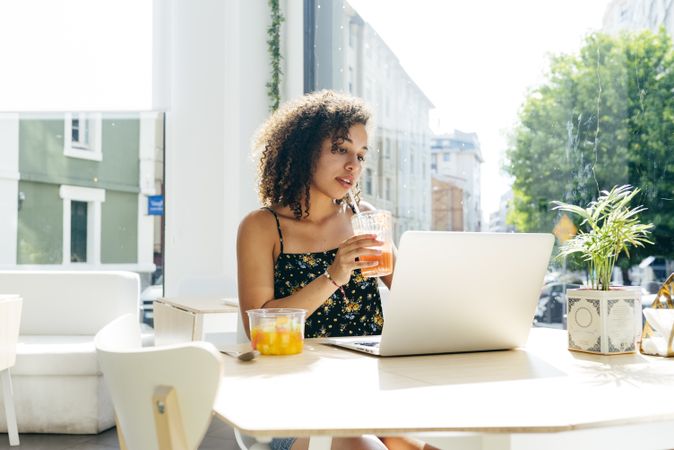 hispanic female with laptop enjoying healthy drink in cafe