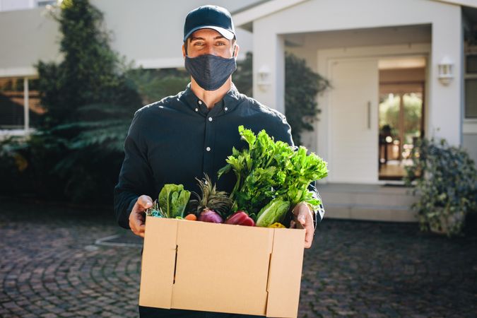 Delivery employee wearing a face mask and holding grocery box outside