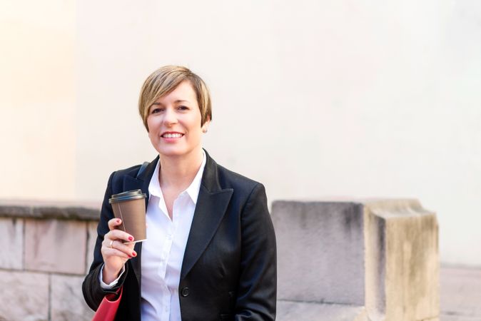 Smiling female in blazer sitting outside with coffee