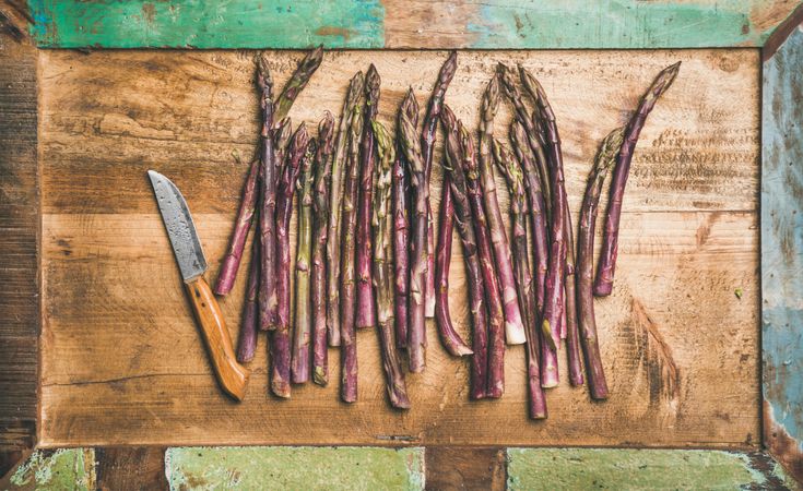 Scattered pieces of washed purple asparagus, on green trimmed wooden board