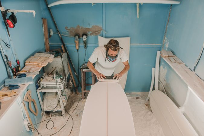 Man in respirator polishing surf board in workshop