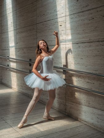 Ballerina doing ballet posing at rail in classroom