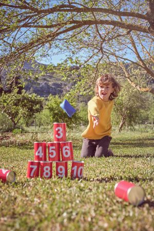 Cheerful kid playing can knockdown game in garden