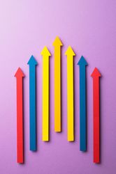 Colorful paper arrows pointing in the same direction on purple background