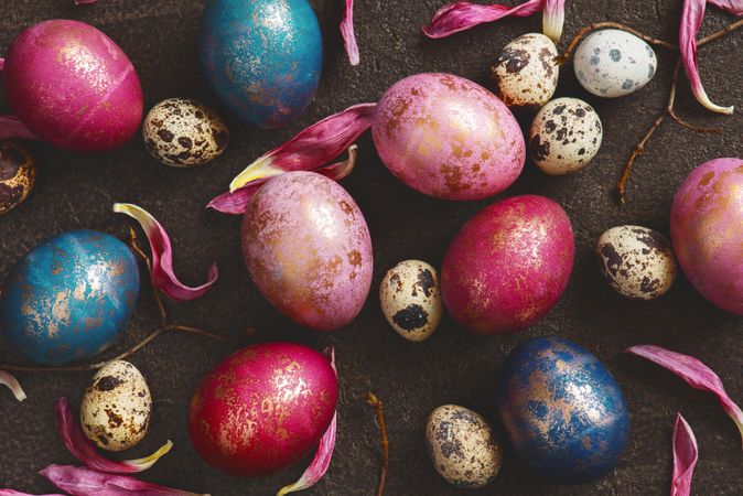 Top view of pink and gold eggs mixed with quail eggs and petals on dark background