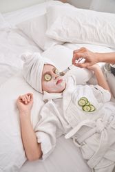 Unrecognizable woman applying facial mask on child