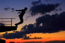 Silhouette side view of male at sunset jumping off roof