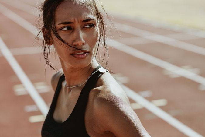 Confident female athlete standing on track and looking away