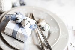 Wrapped Christmas present with bell and star ornament on table setting