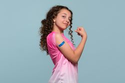 Girl flexing arm with blue bandage after vaccination