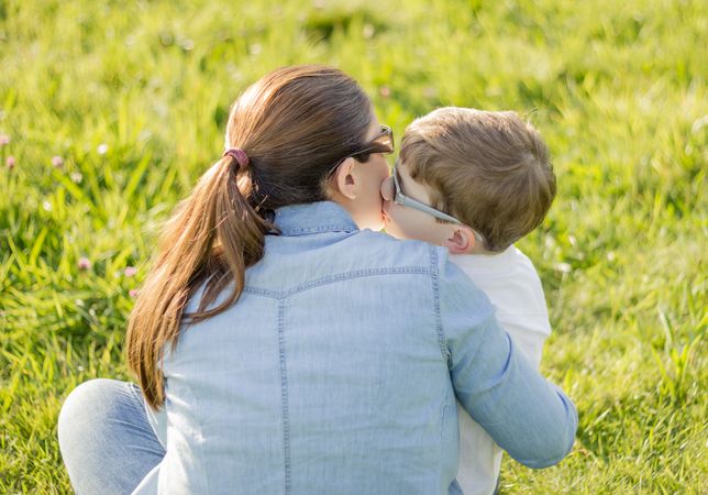 Cute son kissing to his mother sitting in a field
