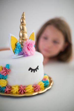 Bright unicorn cake for pleased girl at table