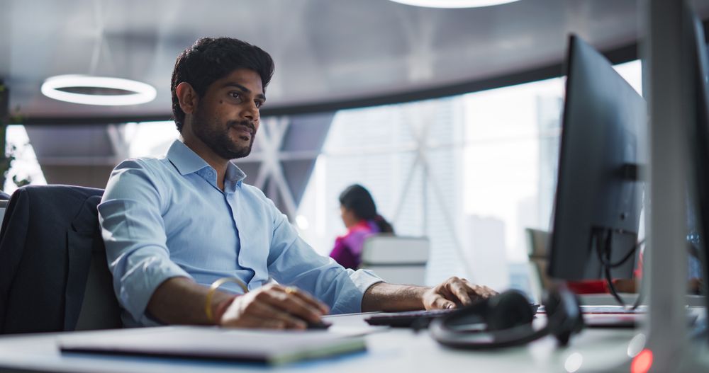 Portrait of a South Asian Financial Securities Trader Working on Desktop Computer in a Modern Office.