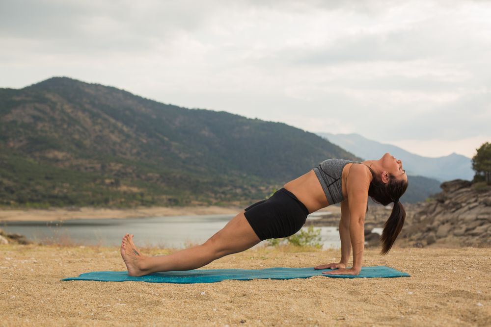 Woman practicing yoga outdoors near water