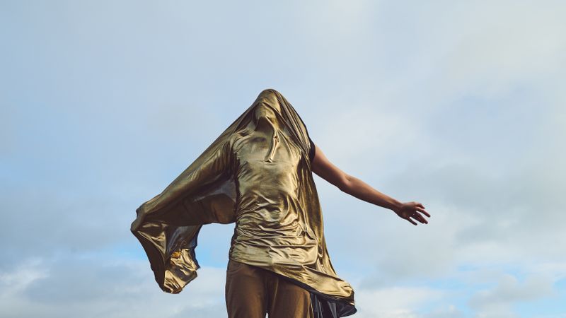 Man draped in gold fabric standing against the wind