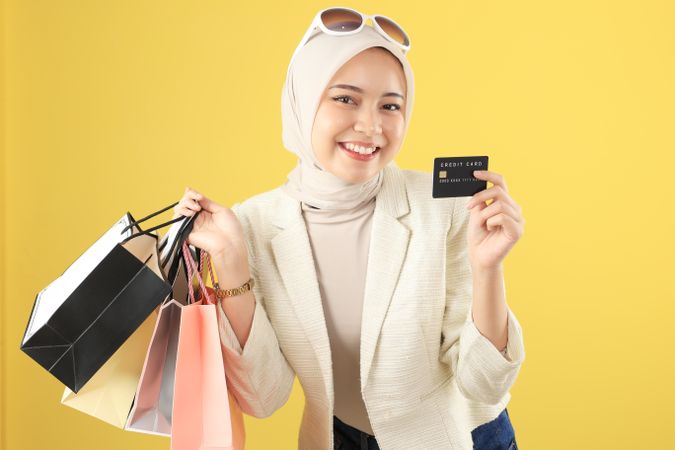 Cheerful Young Asian Muslim Woman Holding Credit Card and Shopping Bags