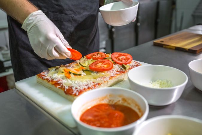 Anonymous male preparing vegetarian pizza with healthy ingredients in a restaurant kitchen
