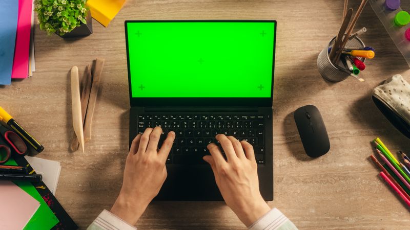 Anonymous Designer Typing on a Laptop with Mock Up Green Screen Chromakey Display with Motion Tracker Placeholders. Illustrator Using a Computer, Working on a Digital Art Portfolio. Top Down View