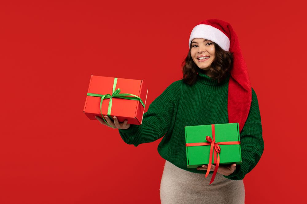 Smiling woman in Santa hat presenting Christmas gift boxes.