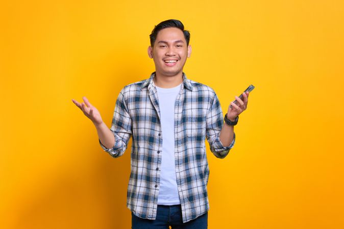 Smiling Asian male with both hands up in the air holding phone