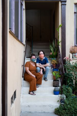 Man and woman sitting on stairs in front of apartment looking at camera