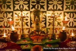 Buddha figurine surrounded by diyas and flowers on a table 0yG8O4
