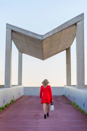 Back of woman in red coat walking towards modern gazebo