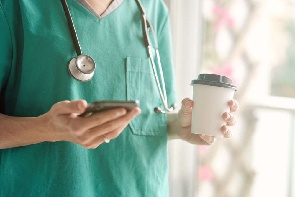 Crop surgeon with smartphone and coffee to go during break