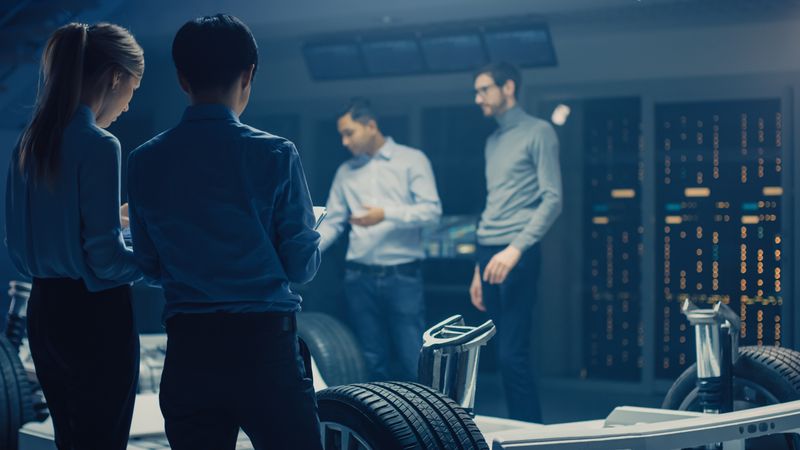 Automobile Engineers Discussing and Designing Electric Car Chassis Platform, Using Tablet Computers with 3D CAD Software