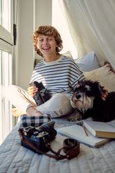 Happy schoolboy with old photo camera and dog on bed