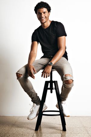 Smiling male model sitting on stool in studio shoot