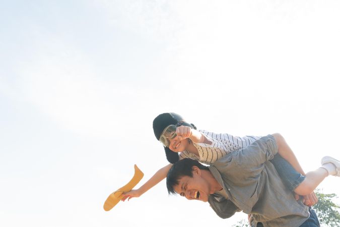 Father giving son piggy back while he’s playing with toy plane in public park