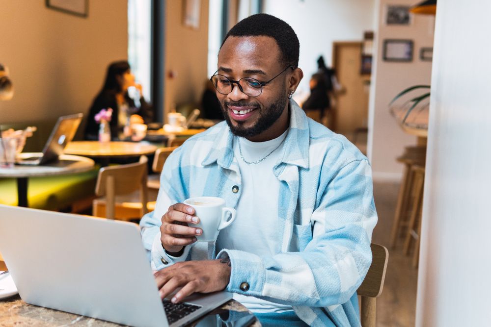 Delighted Black man with coffee browsing laptop