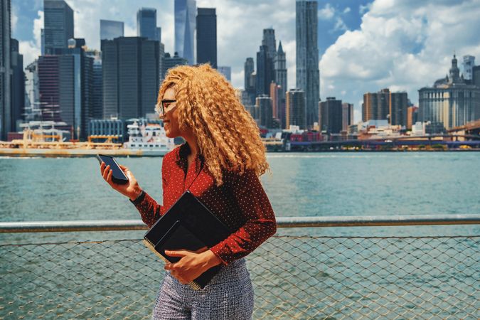Happy professional Black female looking at smart phone by Hudson River